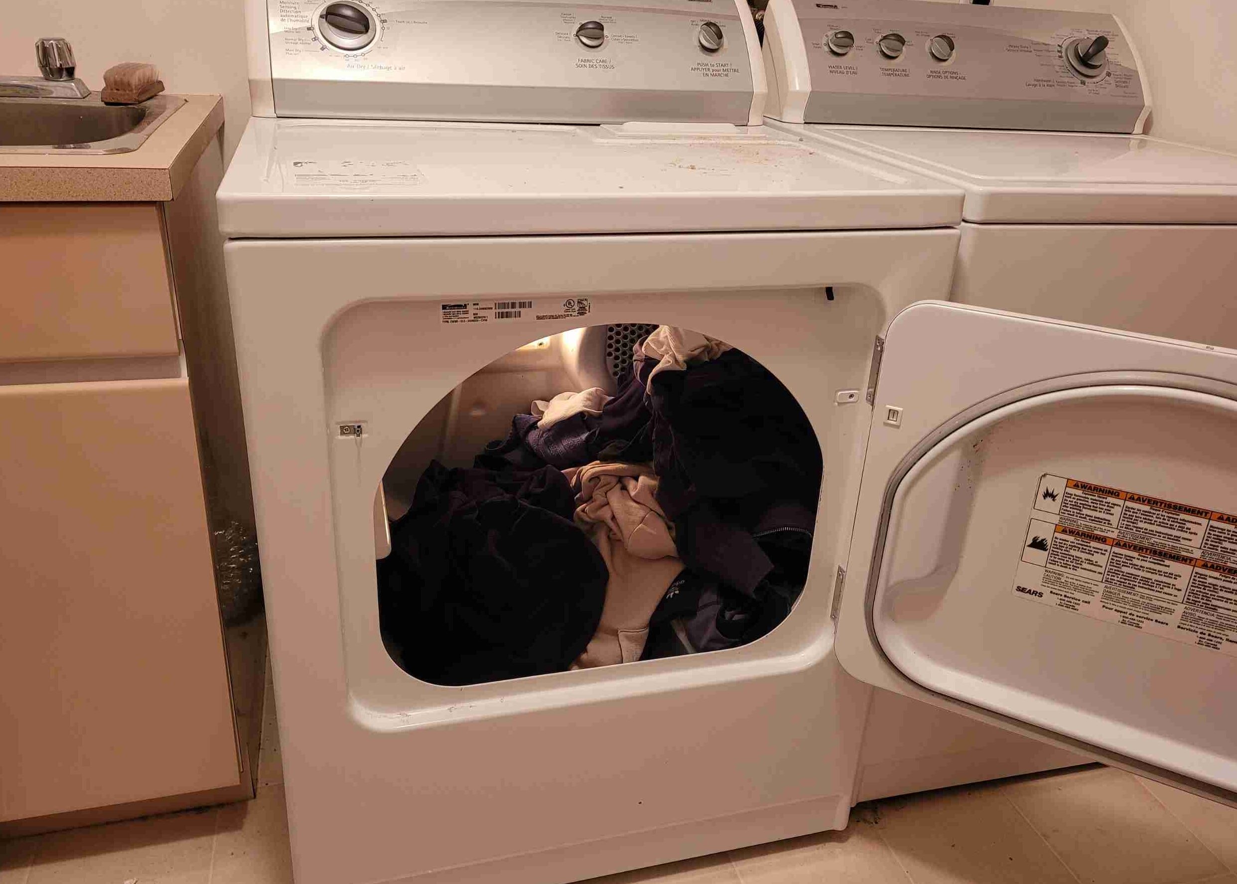 A close-up of a clothes dryer with warm-toned laundry inside. The caption reads, "Exploring dryer temperatures: Unveiling the Heat and understanding how hot dryers can get."